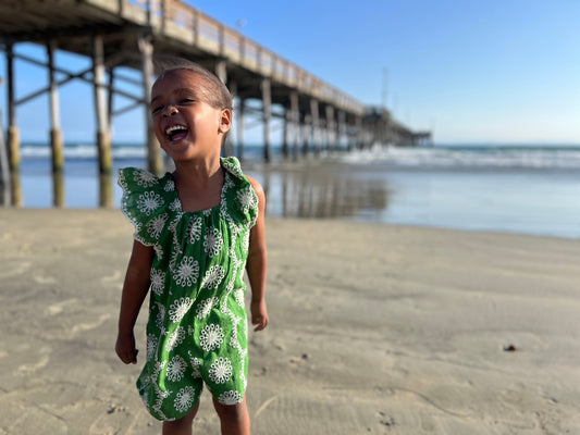 Little girl laughing on the beach while wearing a green eyelet jumpsuit