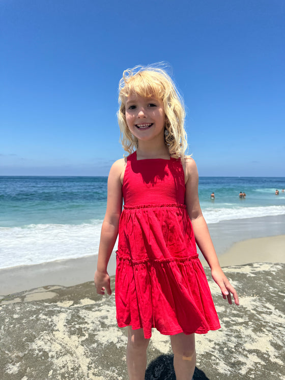 A smiling girl playing at the beach in a bright red patriotic sun dress