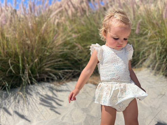 toddler enjoying a fun day at the beach while wearing a white paste flora print skirted bloomer and matching onesie.