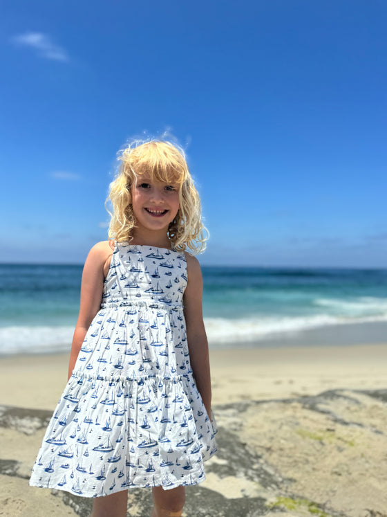 A smiling girl modeling the Sloane dress in all over blue nautical boat print 