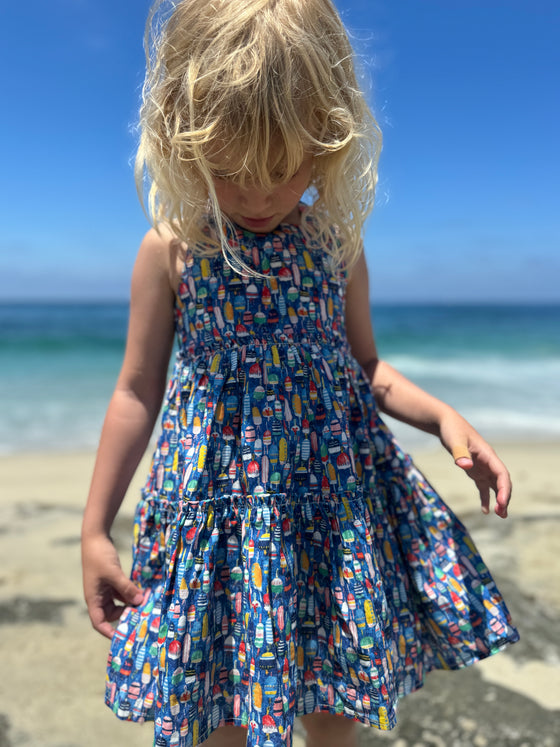 An upclose view of a toddler wearing a blue sun dress with all over colorful nautical buoy print.
