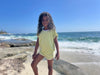 a young girl plays on the beach while wearing a matching Terry print top and shorts in lime green.