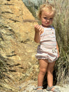 A child model wearing the Karter onesie in natural retro stripe paired with the Remi bloomer in natural retro stripe