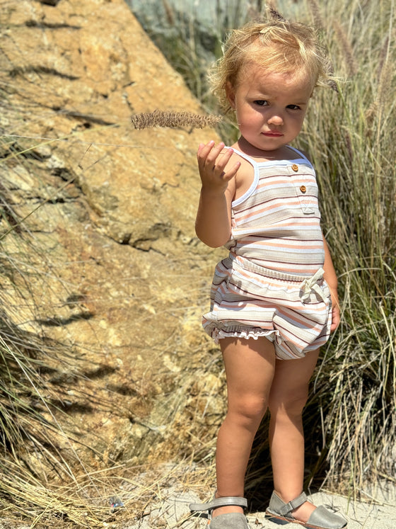 A child model wearing the Karter onesie in natural retro stripe paired with the Remi bloomer in natural retro stripe