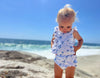 A toddler having a fun day at the beach wearing a white and blue floral baby bloomer and matching onesie 