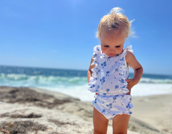 A toddler having a fun day at the beach wearing a white and blue floral baby bloomer and matching onesie 