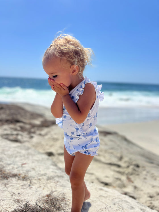 A darling baby girl playing on the beach while wearing a white and blue baby bloomer with matching baby onesie 