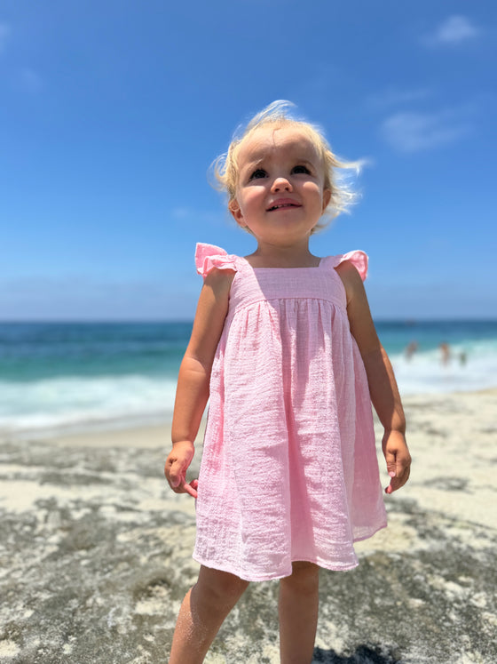Girl toddler playing on the beach in pink dress with ruffled sleeves 