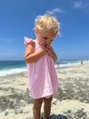 Girl toddler looking down while  playing on the beach in pink dress with ruffled sleeves 