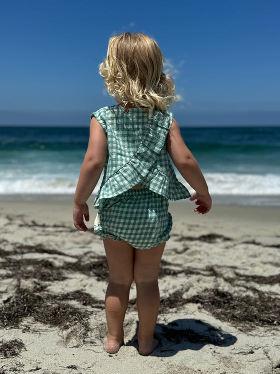 Child model on the beach wearing Green Plaid Aria dress with matching bloomer showing back view with riffle criss-cross detail.  