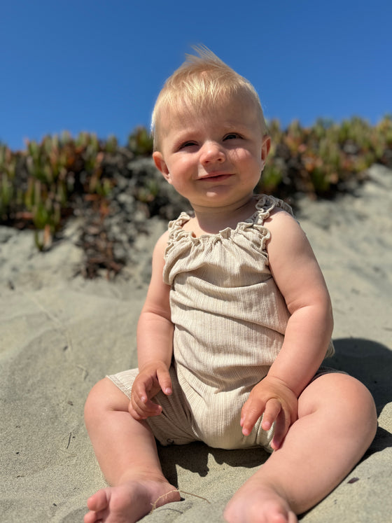 Smiling blond haired baby wearing oatmeal ruffled romper