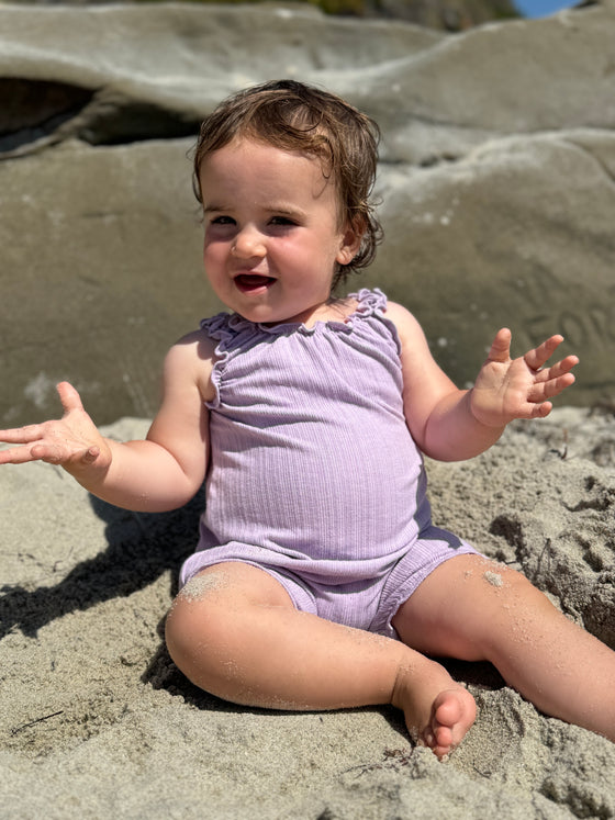 Baby girl model smiling at the beach while wearing a lavender bubble 