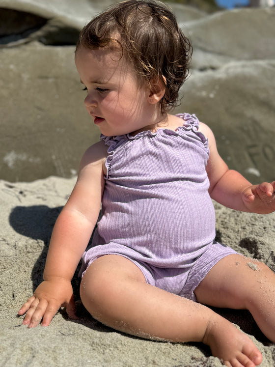 Baby girl wearing purple romper while playing at the beach
