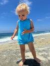 a baby girl model at the beach wearing a bright blue romper