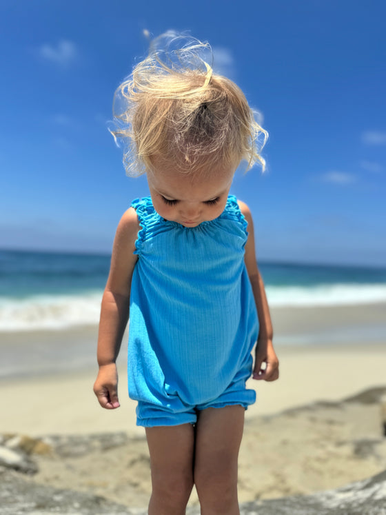 Sweet baby girl model looking down at her feet while wearing a bright blue romper