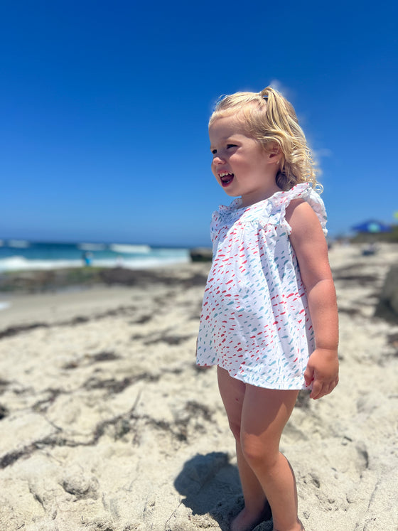 Child model wearing the Jenn Dress in Coral and Aqua School of fish print while playing at the beach