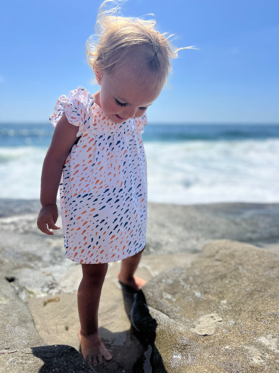 Toddler model enjoying a day at teh beach wearing the Jenn Dress with Blue nad orange school of fish print 