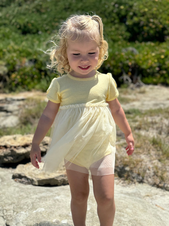 Blond haired girl playing on the beach in a yellow tulle ballerina dress