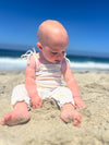 Baby playing at the beach in a striped blue and yellow romper