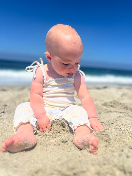 Baby playing at the beach in a striped blue and yellow romper