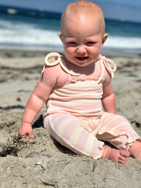 Baby playing on the beach wearing a ribbed stripe yellow and pink romper