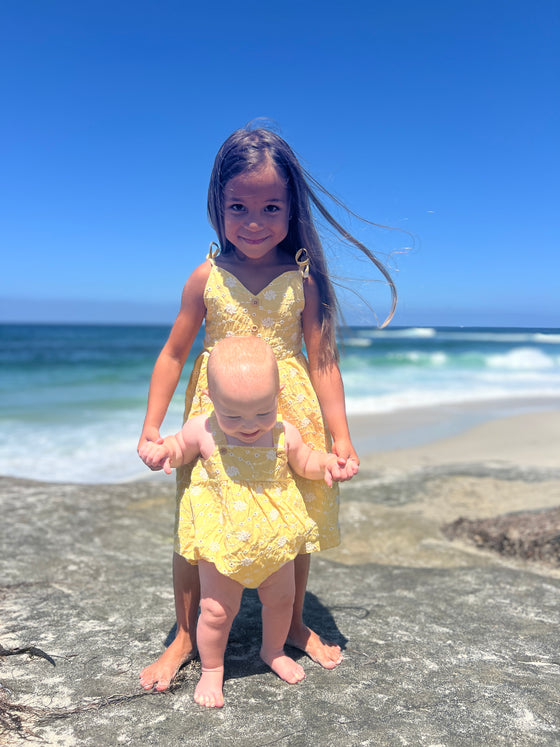 two sisters enjoying a day at the beach while wearing matching outfits both in yellow dandelion print.  