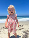 Blond toddler on the beach wearing a pink floral romper
