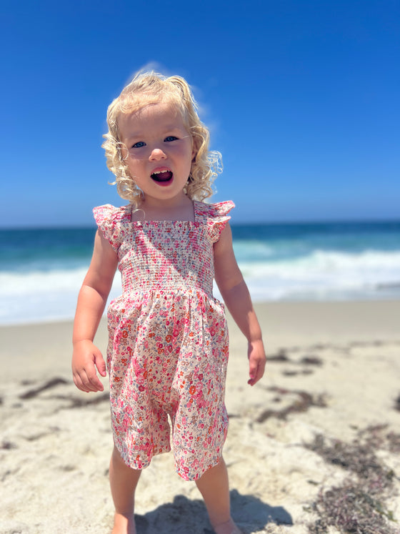 Blond toddler on the beach wearing a pink floral romper