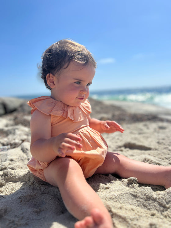 Baby playing on beach in orange ruffled romper 
