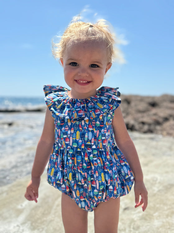 “Toddler wearing Vignette’s Maya bubble romper in nautical buoy print, enjoying a sunny day at the beach. This stylish and comfortable baby outfit is perfect for seaside adventures and summer fun. Shop this adorable coastal-inspired bubble for your little one’s wardrobe.”