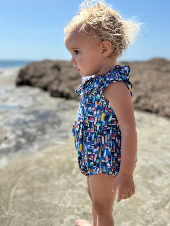 Toddler wearing Vignette’s Maya bubble romper in nautical buoy print, enjoying a sunny day at the beach. This stylish and comfortable baby outfit is perfect for seaside adventures and summer fun. Shop this adorable coastal-inspired bubble for your little one’s wardrobe.