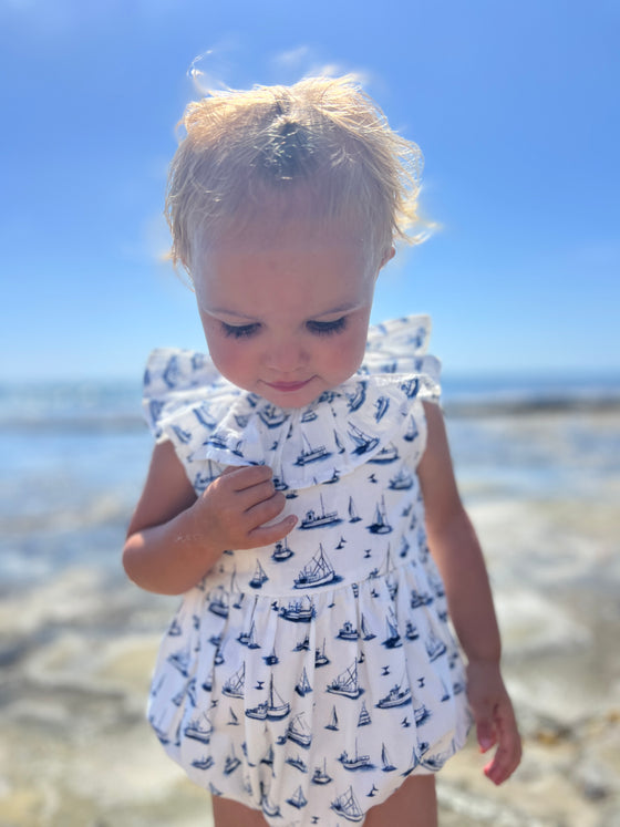 This beach day features a little one dressed in the Vignette Maya romper with a nautical boat design, an ideal outfit for summer play and coastal charm.