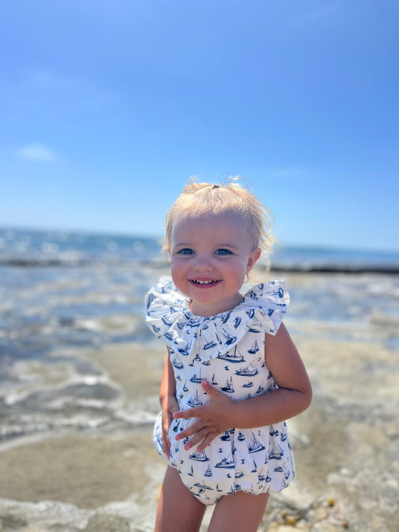 A toddler enjoys a sunny day on the beach wearing Vignette’s Maya romper in nautical boats, a perfect choice for seaside adventures and warm weather fun.
