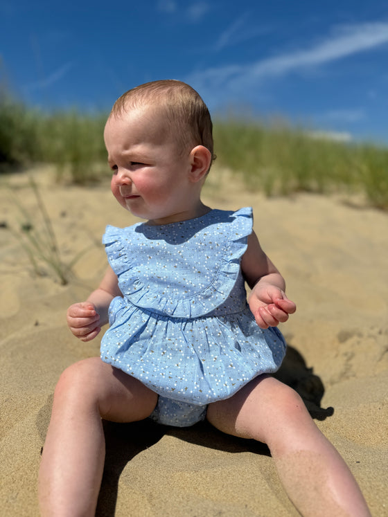 Baby girl enjoying a day at the beach while wearing a pale blue ruffled floral patterned onesie