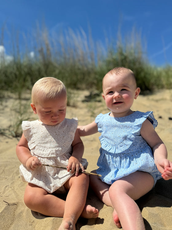 Two baby girls on the beach wearing matching carrie bubbles on in oatmeal and the other in blue