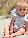 A blonde baby girl plays in the sand, wearing the Cammie Bubble in Pink and Blue Multi Stripe. With flutter sleeves and a playful multi-stripe design, this baby bubble romper is perfect for beach outings. The breathable fabric keeps her cool while the vibrant pink and blue stripes ensure she looks cute and stylish all day long.