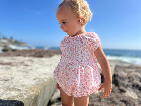 a baby wearing a white bubble with a coral floral print pattern.  
