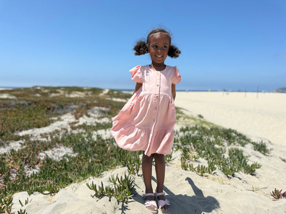 A young girl proudly showing off her pale pink tiered peasant dress while standing on a sand dune.  