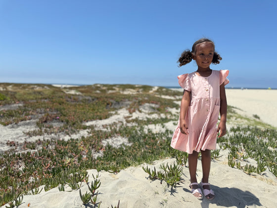 Young girl playing on san dunes while wearing a pale pink flutter sleeve dress