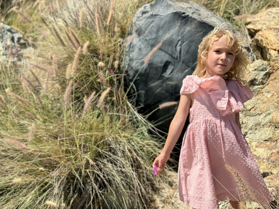 a young girl plays on sand dunes while wearing a pale pink ruffled sun dress 