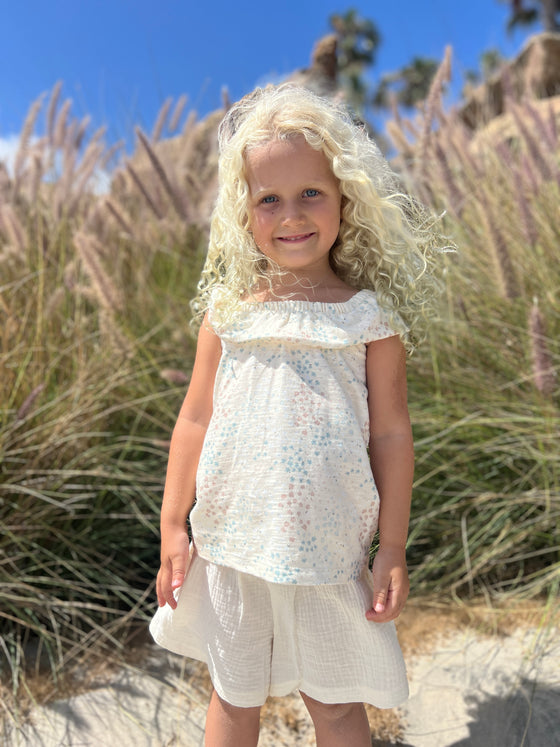 Smiling little girl model wearing a ruffled tee with delicate floral print and matching white skort 