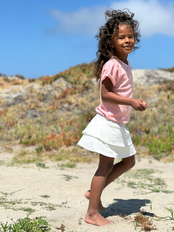 a little girl runs on the beach while waring a pale pink terry cloth shirt and white peasant skirt