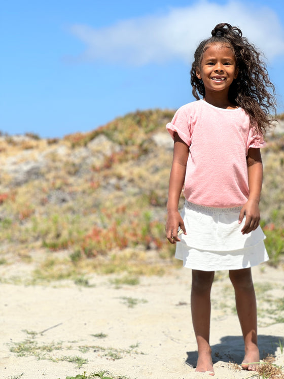 A little girl plays on the sand dunes while wearing a pink Terry cloth shirt nad white tiered skort